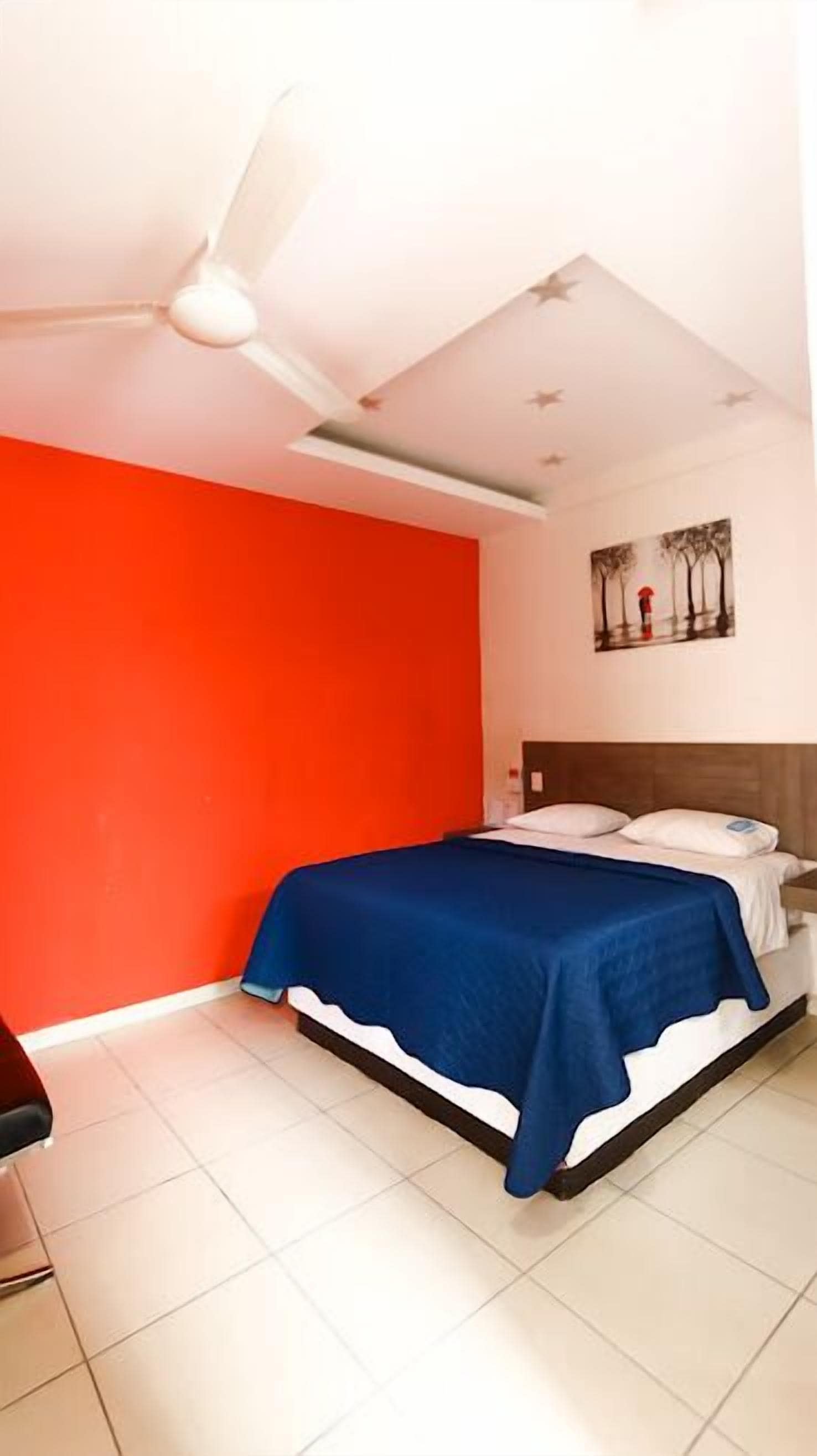 Ein Schlafzimmer mit einem Bett, einem Deckenventilator, einer roten Wand und einem Gemälde an der Wand.