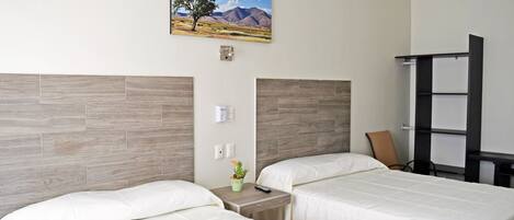 Habitación de hotel con dos camas, un cuadro de un paisaje, una mesita con una planta y una silla.