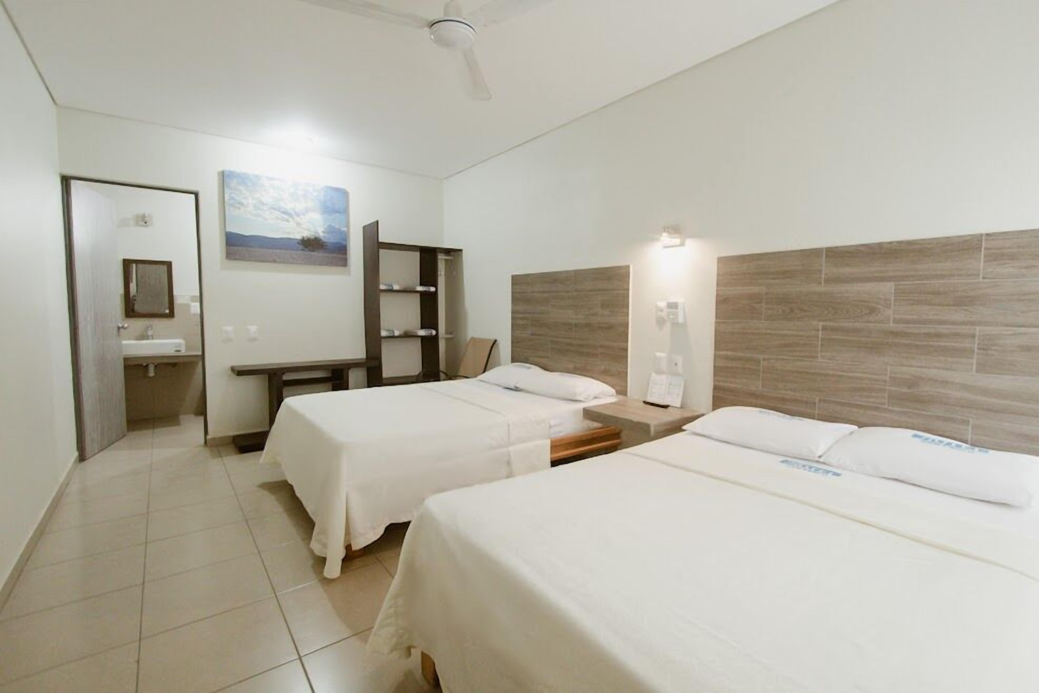 Ein Hotelzimmer mit zwei Betten, einem Badezimmer, einem Schreibtisch und einem Bild an der Wand.