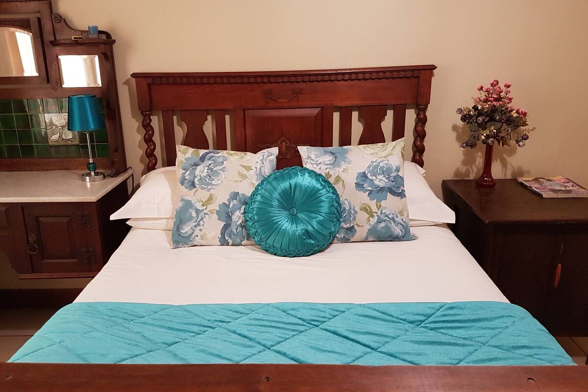 A neatly made bed with a floral pillow and a teal blanket.