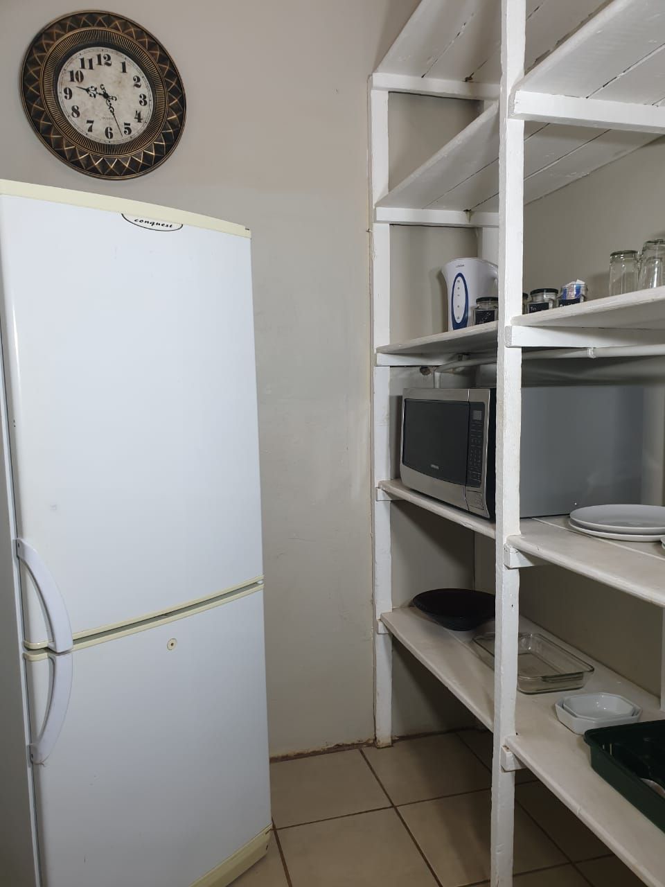 Uma cozinha com geladeira branca, micro-ondas e prateleiras com diversos utensílios.