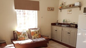 A cozy room with a sofa, a small table, a kitchen area with cabinets, a refrigerator, and a window with blinds. - Misty Mountains (Studholme)