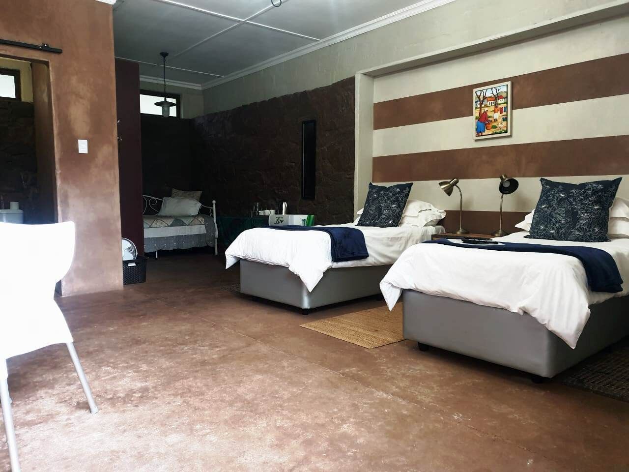 A hotel room with two beds, a white chair, and a painting on the wall.