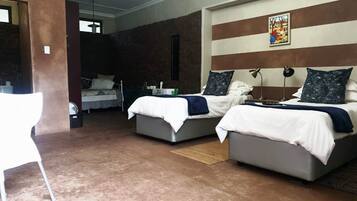 A hotel room with two beds, a white chair, and a painting on the wall.