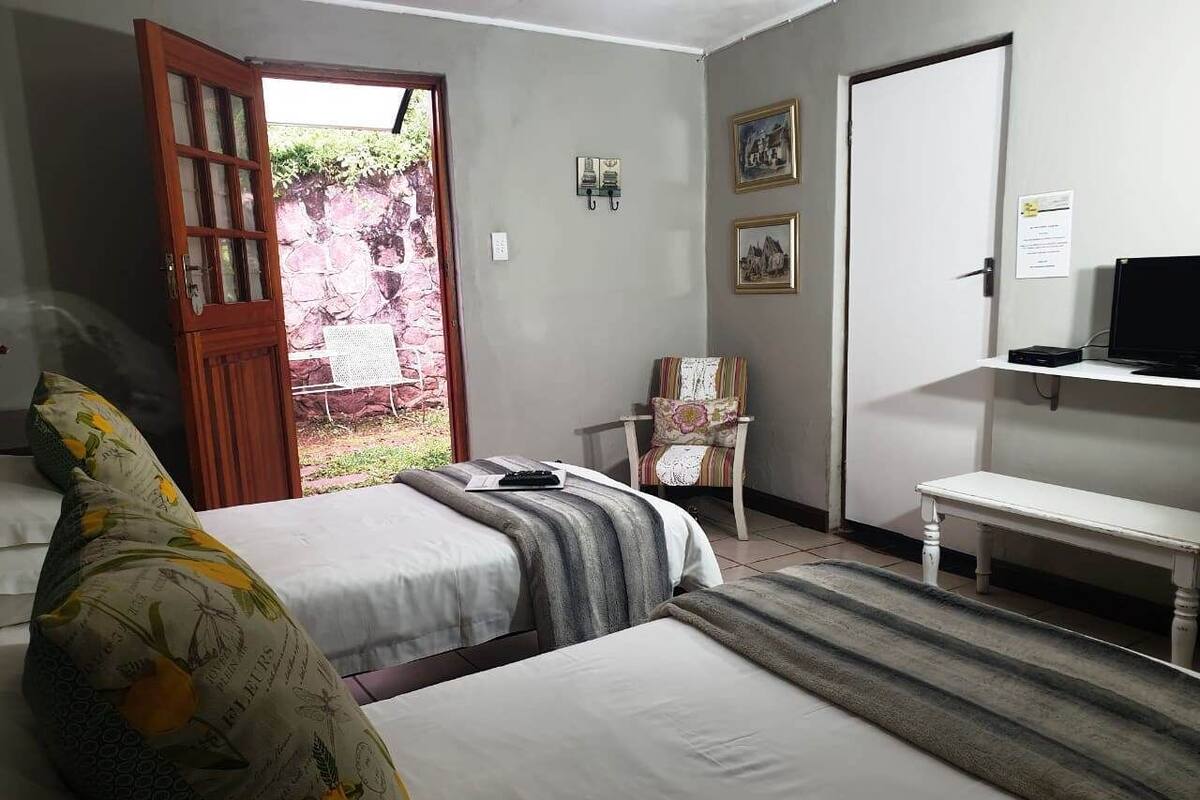 A bedroom with two beds, a chair, a bench, a door, and a small shelf with a laptop.