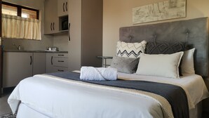 Un dormitorio con una cama grande, un cabecero y una mesita de noche. Cuenta con una kitchenette con armarios y un lavabo.