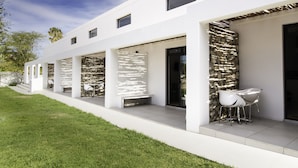 A modern building with a white exterior, large windows, and a covered outdoor seating area with chairs. - Karoo Retreat (Oudtshoorn)