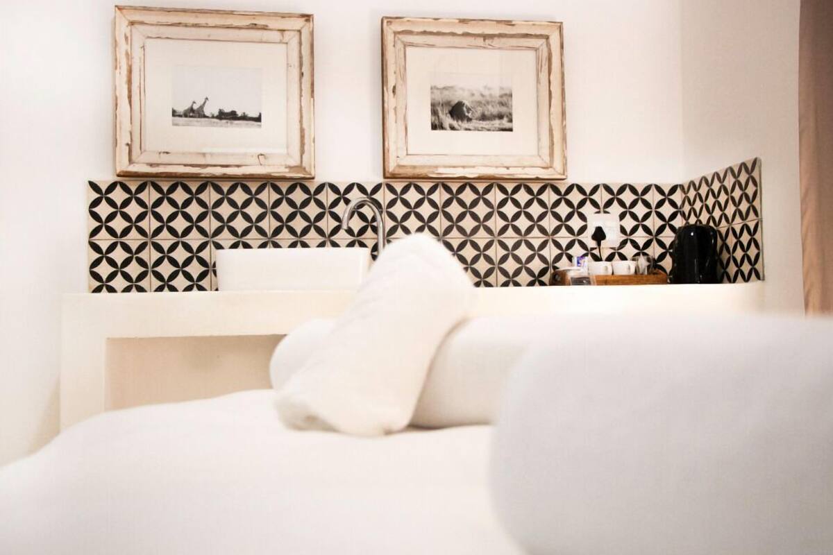Une chambre d’hôtel avec un lit, une table de chevet blanche, un miroir et deux tableaux encadrés accrochés au mur.