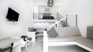 A modern living space with a flat-screen TV mounted on the wall, a dining area with a white table and chairs, a sofa with a striped pillow, and a staircase leading to an upper level. - Karoo Retreat (Oudtshoorn)