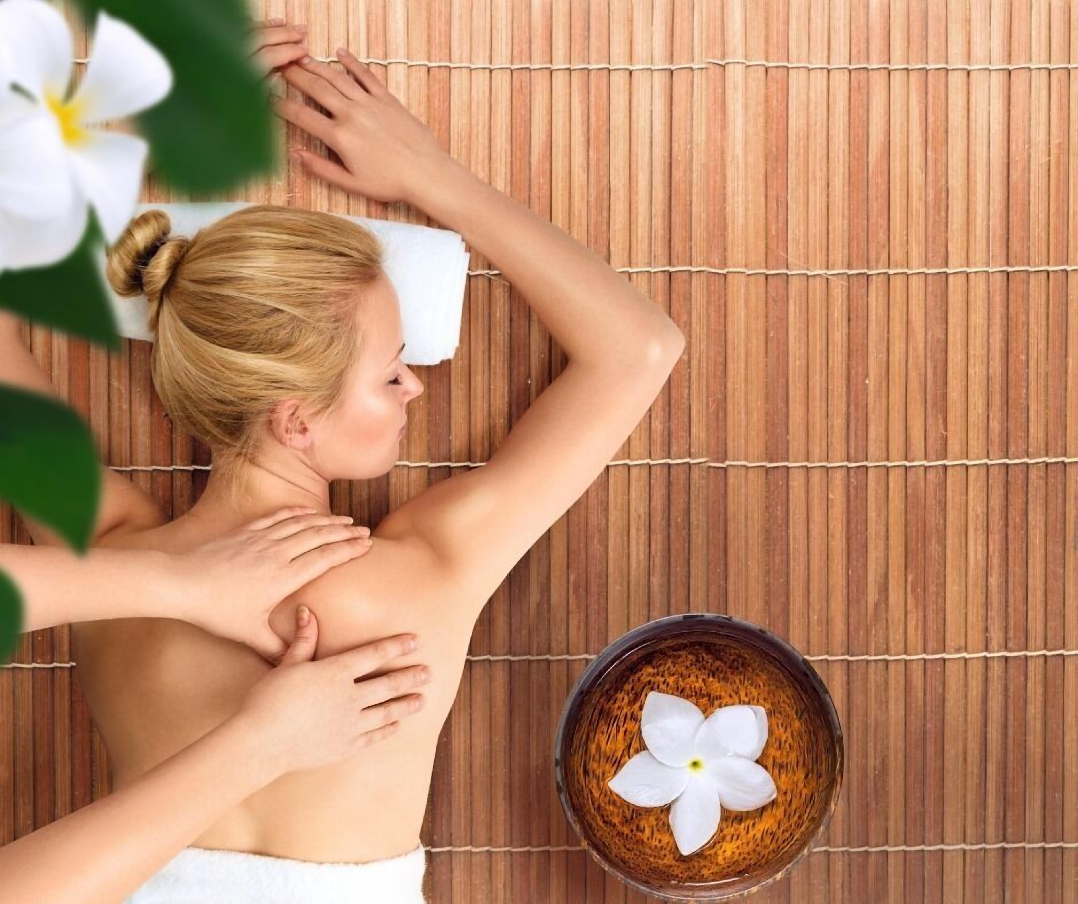 A person receiving a back massage on a bamboo mat with a flower in a bowl nearby.
