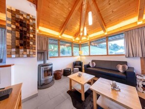 A cozy living room with a fireplace, a sofa, a coffee table, and large windows.