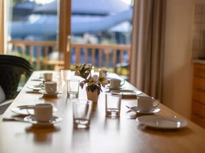 A dining table set with white cups, saucers, and a vase with white flowers.