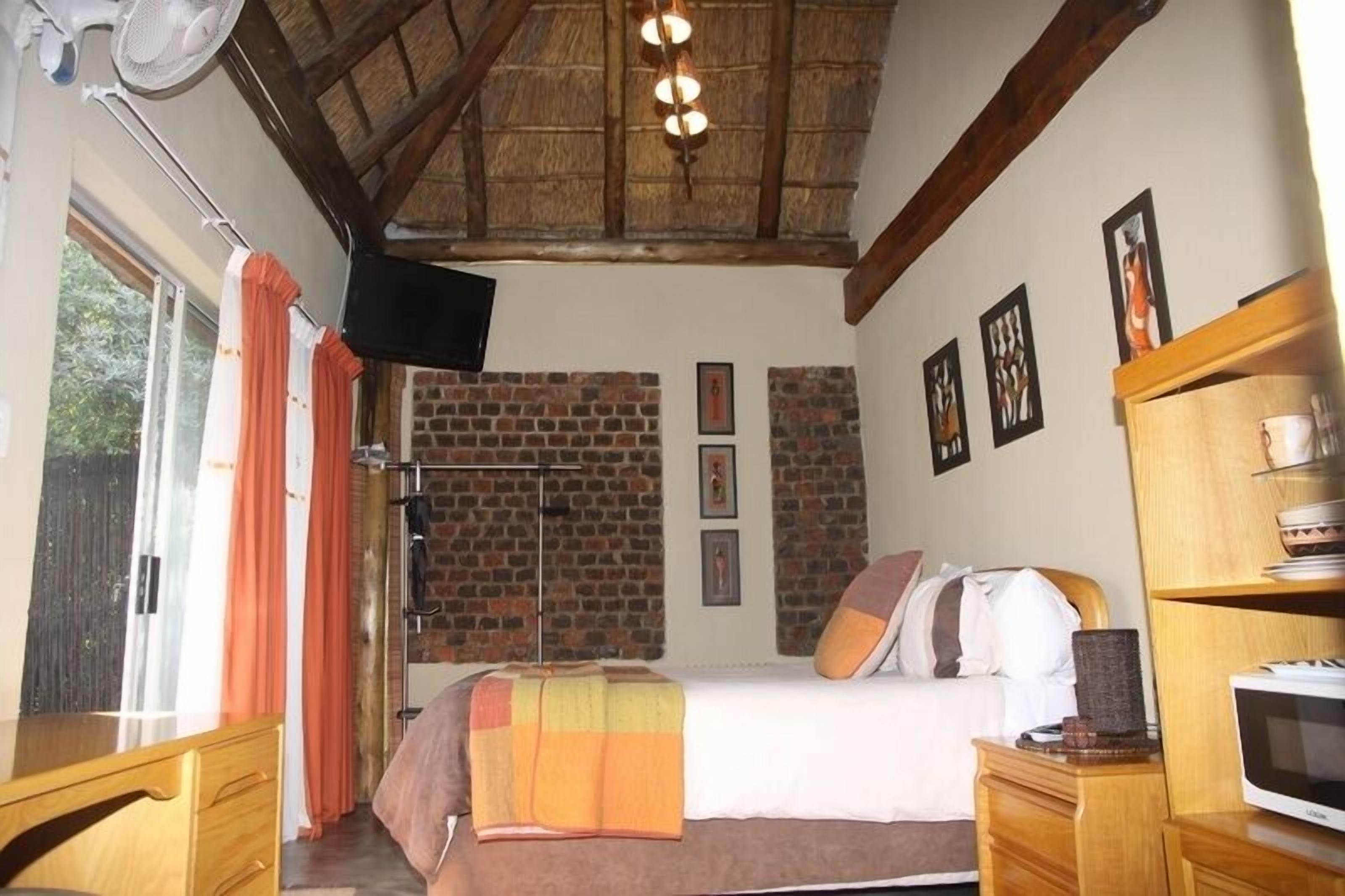 Un dormitorio con pared de ladrillo, una cama con almohadas, un televisor, un aparador de madera y un microondas.