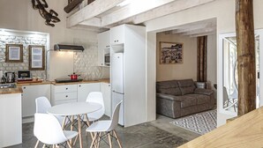Eine kompakte Küche mit weißen Schränken, ein Esstisch mit Stühlen und ein graues Sofa im angrenzenden Wohnbereich.