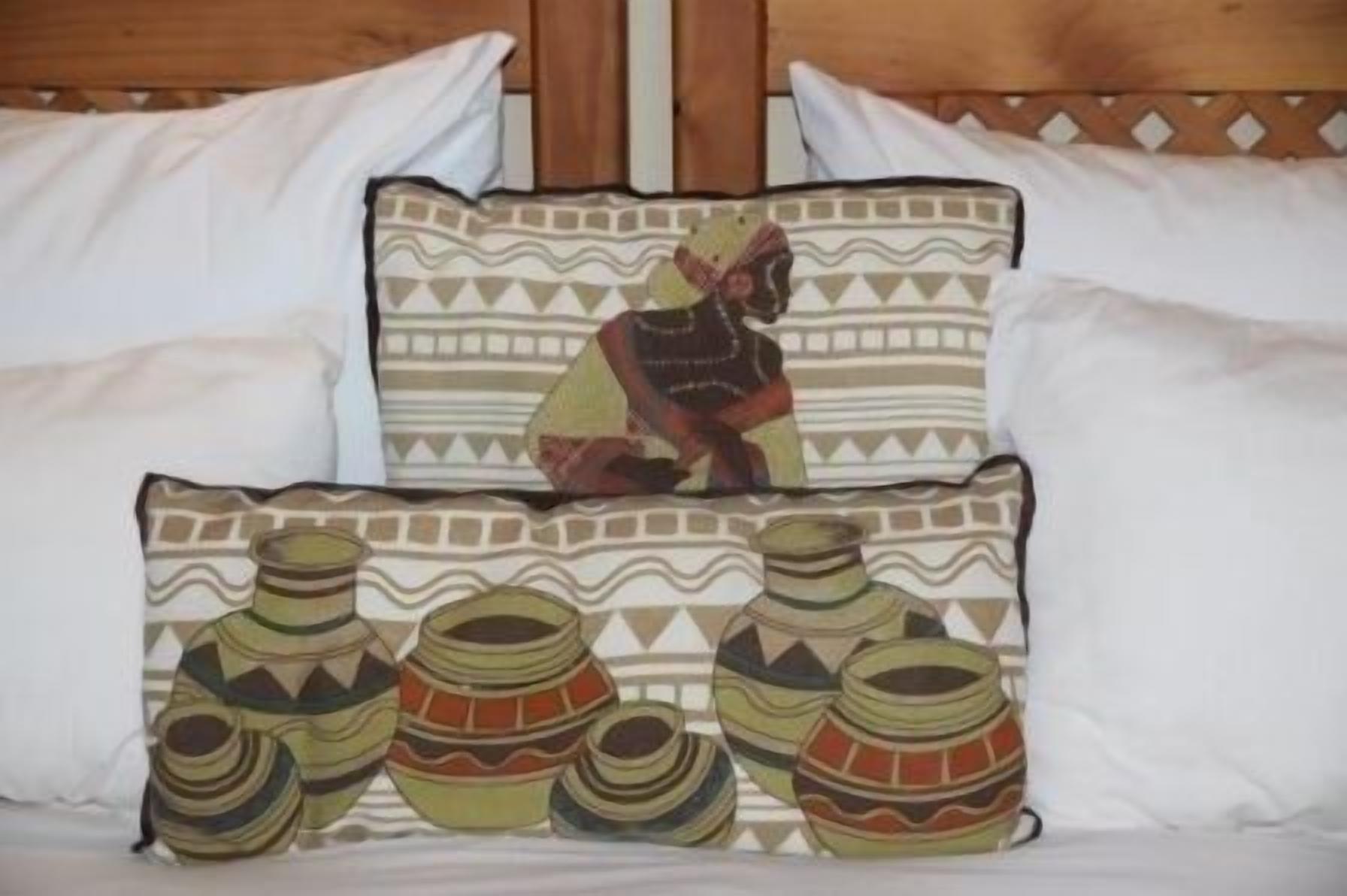 Ein Bett mit zwei dekorativen Kissen, eines mit geometrischem Muster und das andere mit einem kulturellen Design.