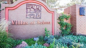 A sign for 'Villas of Sedona' with a decorative emblem, surrounded by lush greenery and a brick structure.