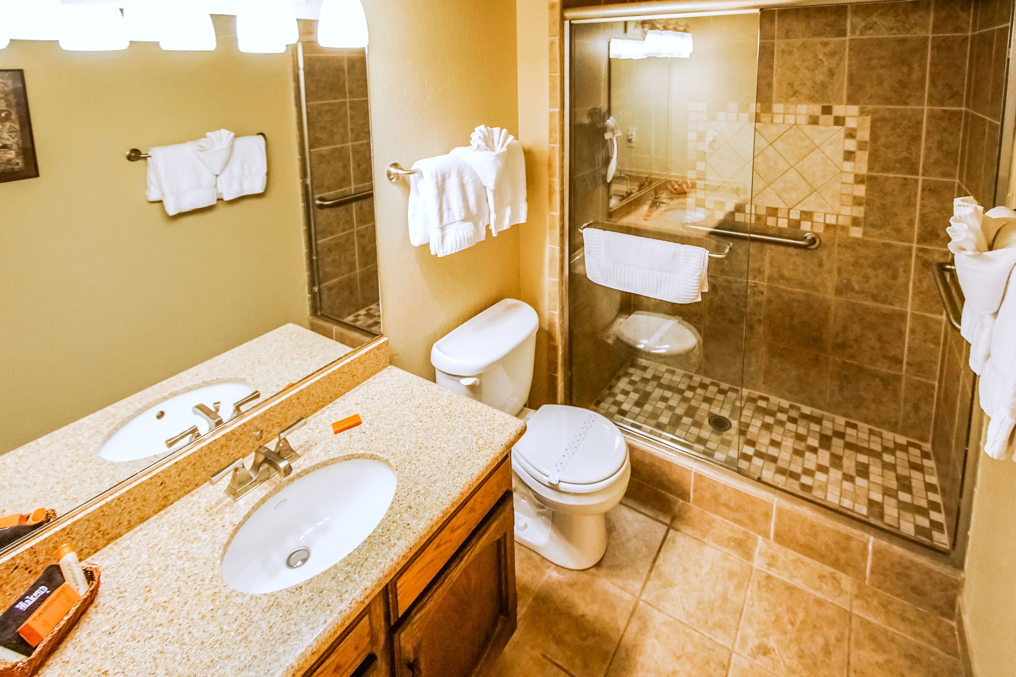 Un baño con dos lavamanos, un inodoro y una zona de ducha con mampara de vidrio.