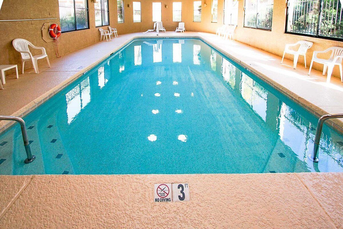 An indoor swimming pool with a 3 ft depth sign, white chairs, and a lifebuoy on the wall.