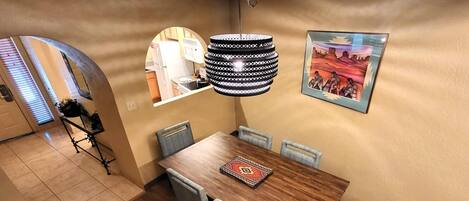Un comedor con una mesa de madera, seis sillas, un tapete estampado, una lámpara colgante y un cuadro en la pared.