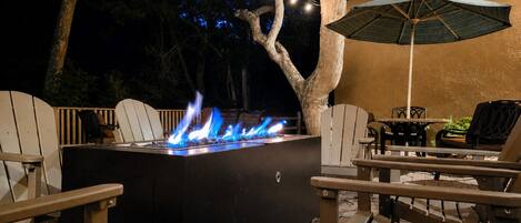An outdoor patio with a built-in fire feature, seating, and string lights.