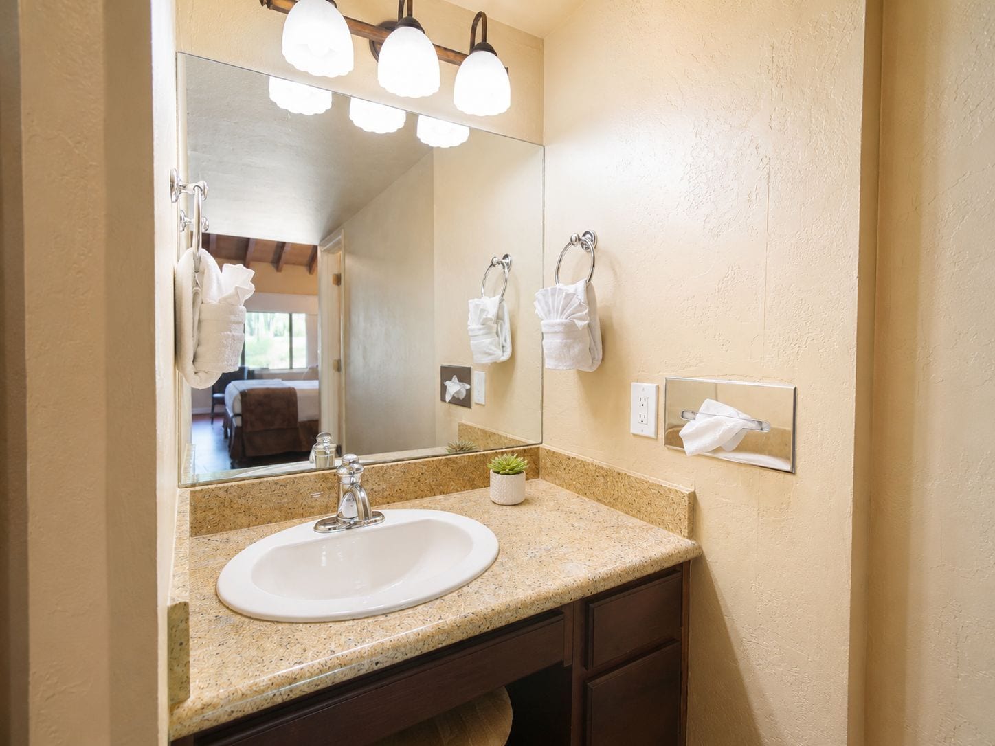 Une salle de bain avec un comptoir en granit, un lavabo blanc, un miroir avec éclairage intégré et un porte-serviettes.
