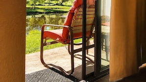 A room with a sliding glass door leading to an outdoor area with a chair and a view of a pond and trees. - Villas At Poco Diablo (Sedona)