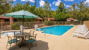 A swimming pool with lounge chairs and a table with chairs, surrounded by a fence and trees. - Villas At Poco Diablo (Sedona)