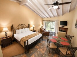 Habitación de hotel con cama, lámparas de noche, sofá, mesa de comedor con sillas, televisor y chimenea.