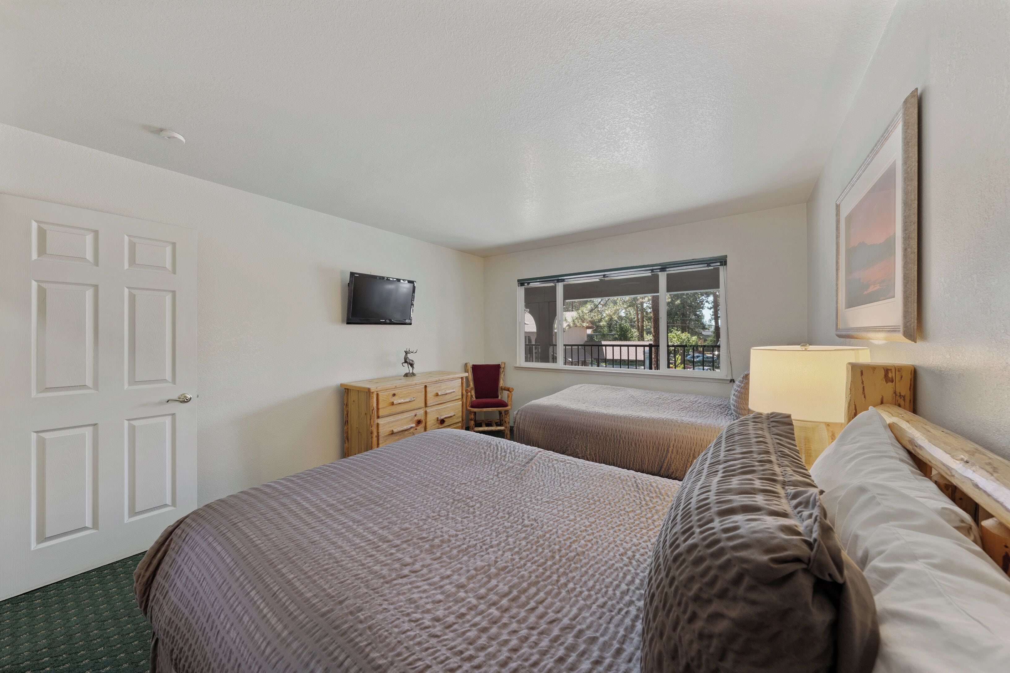 A bedroom with two beds, a television, a window, and a door.