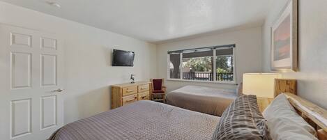 A bedroom with two beds, a television, a window, and a door.