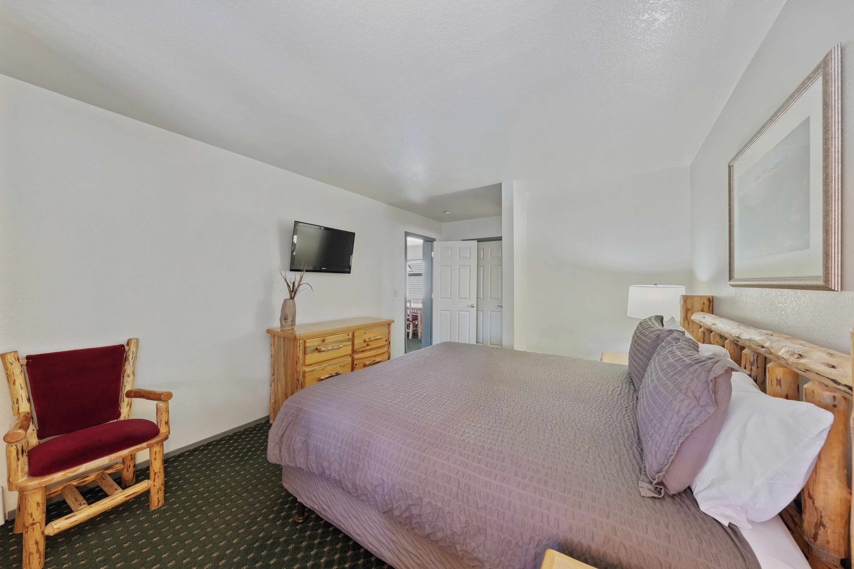 A hotel room with a large bed, a wooden chair, a television, and a dresser.