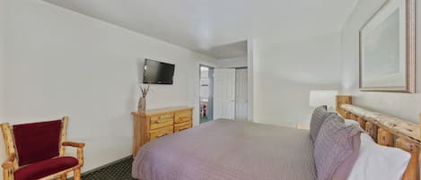 A hotel room with a large bed, a wooden chair, a television, and a dresser.