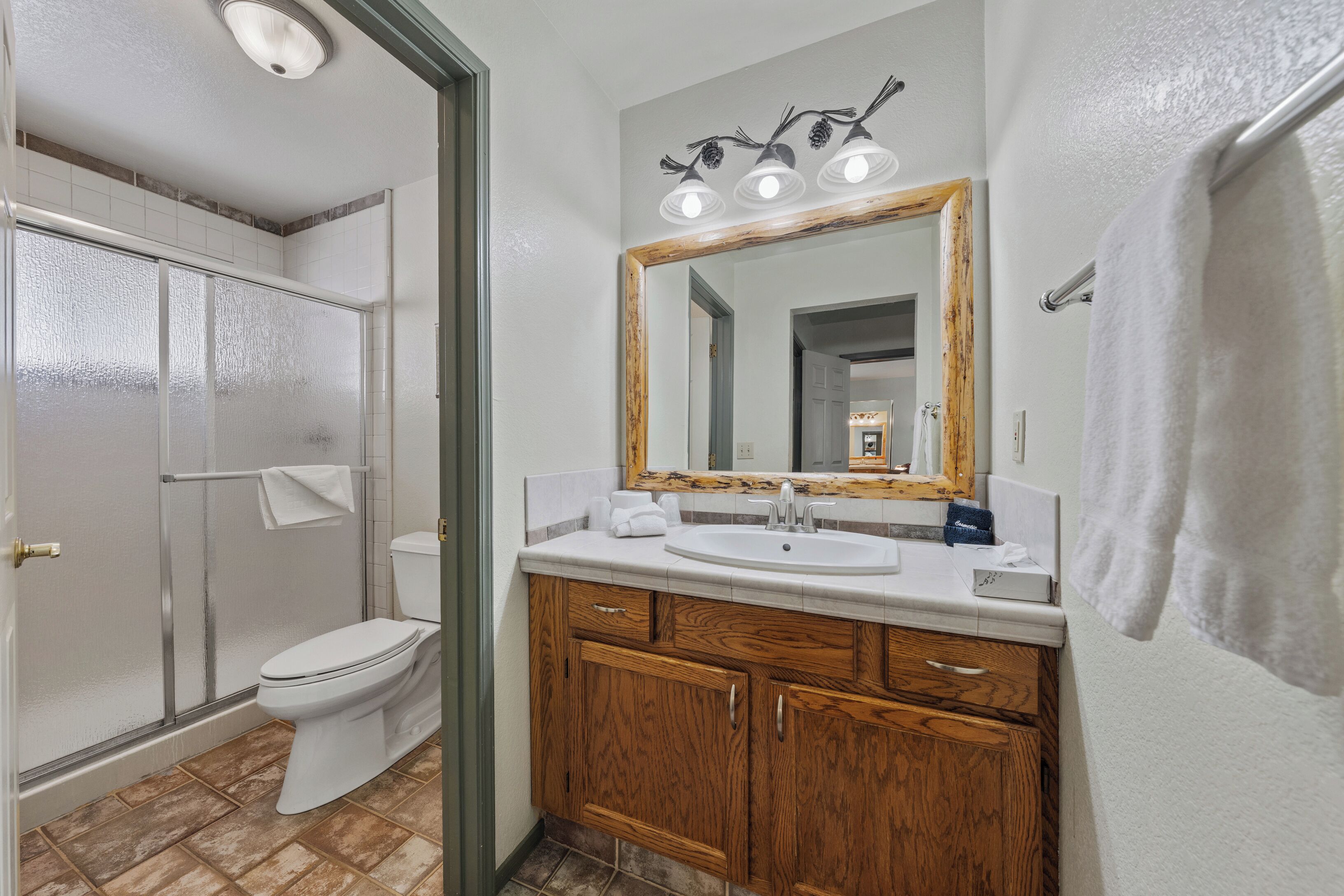 A bathroom with a shower, toilet, sink, and wooden cabinets.