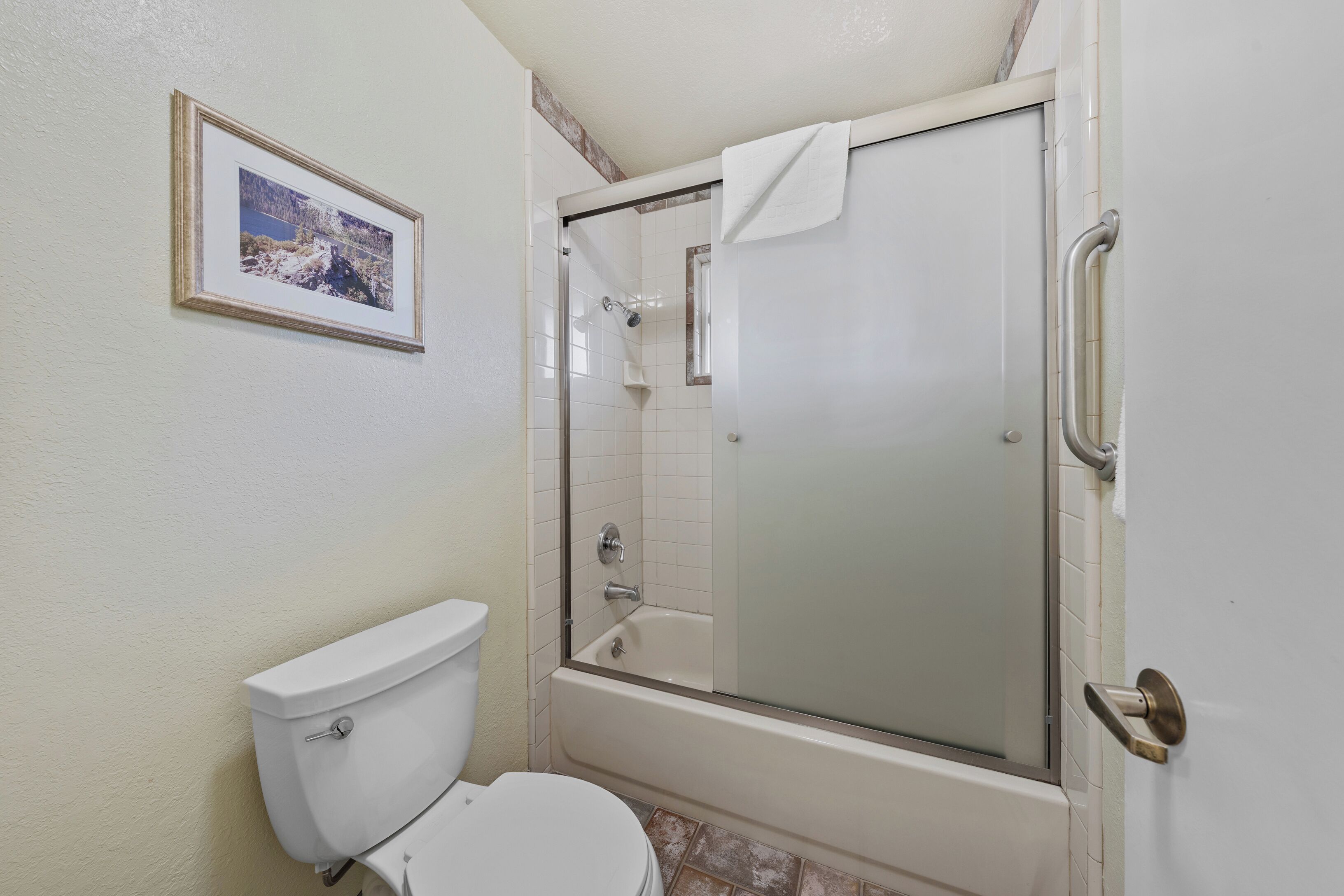A bathroom with a toilet, a glass-enclosed shower, and a framed picture on the wall.