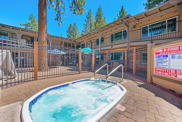 Un área de piscina con jacuzzi, rodeada por una valla, y un edificio con múltiples ventanas y balcones.