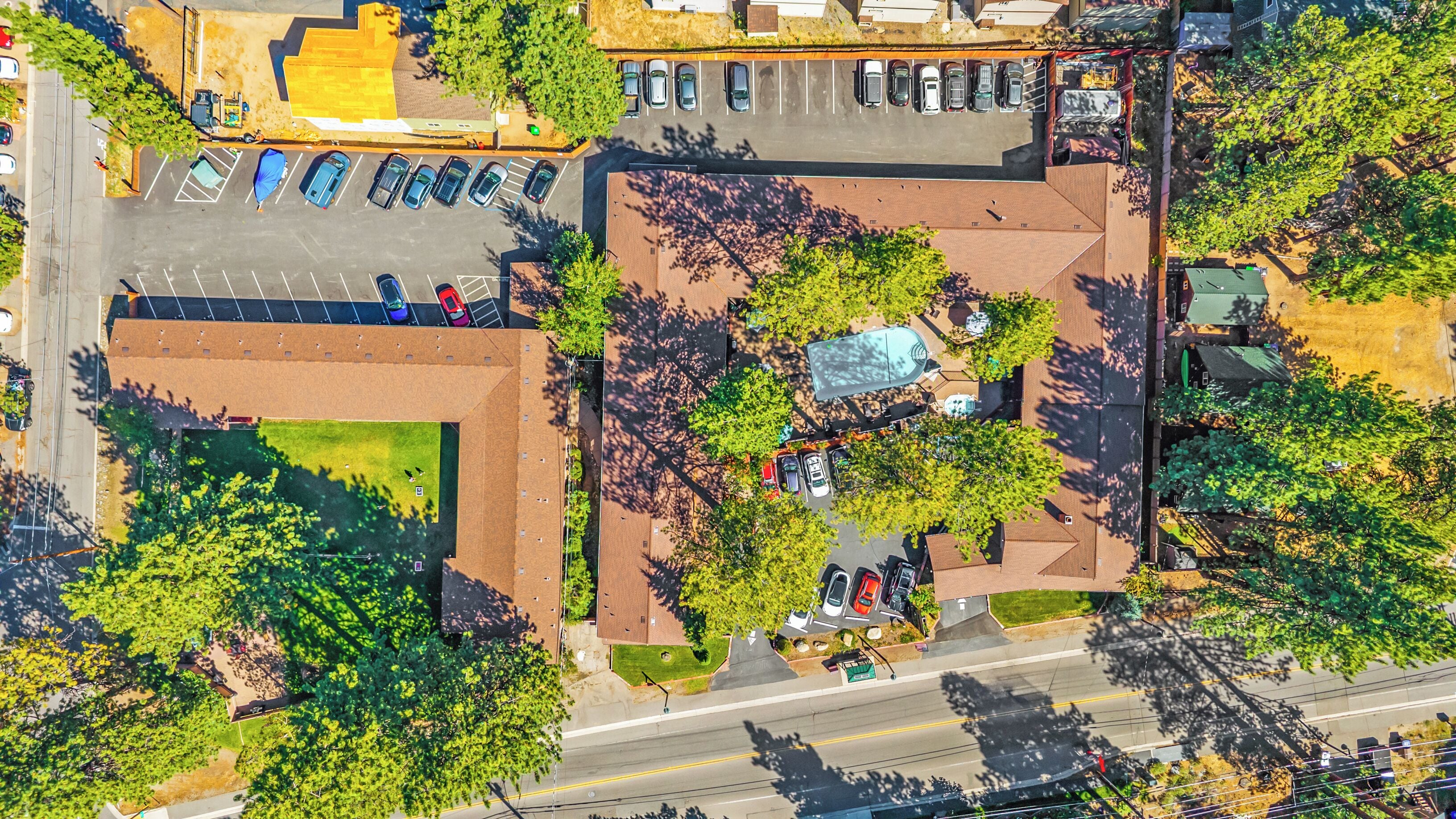 An aerial view of a parking lot with multiple cars, a swimming pool, and surrounding greenery.