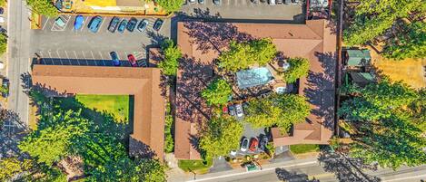 An aerial view of a parking lot with multiple cars, a swimming pool, and surrounding greenery.
