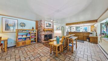 A cozy living area with a fireplace, wooden furniture, and a kitchen in the background.