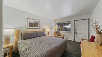 A bedroom with a bed, a chair, a table, and a door.