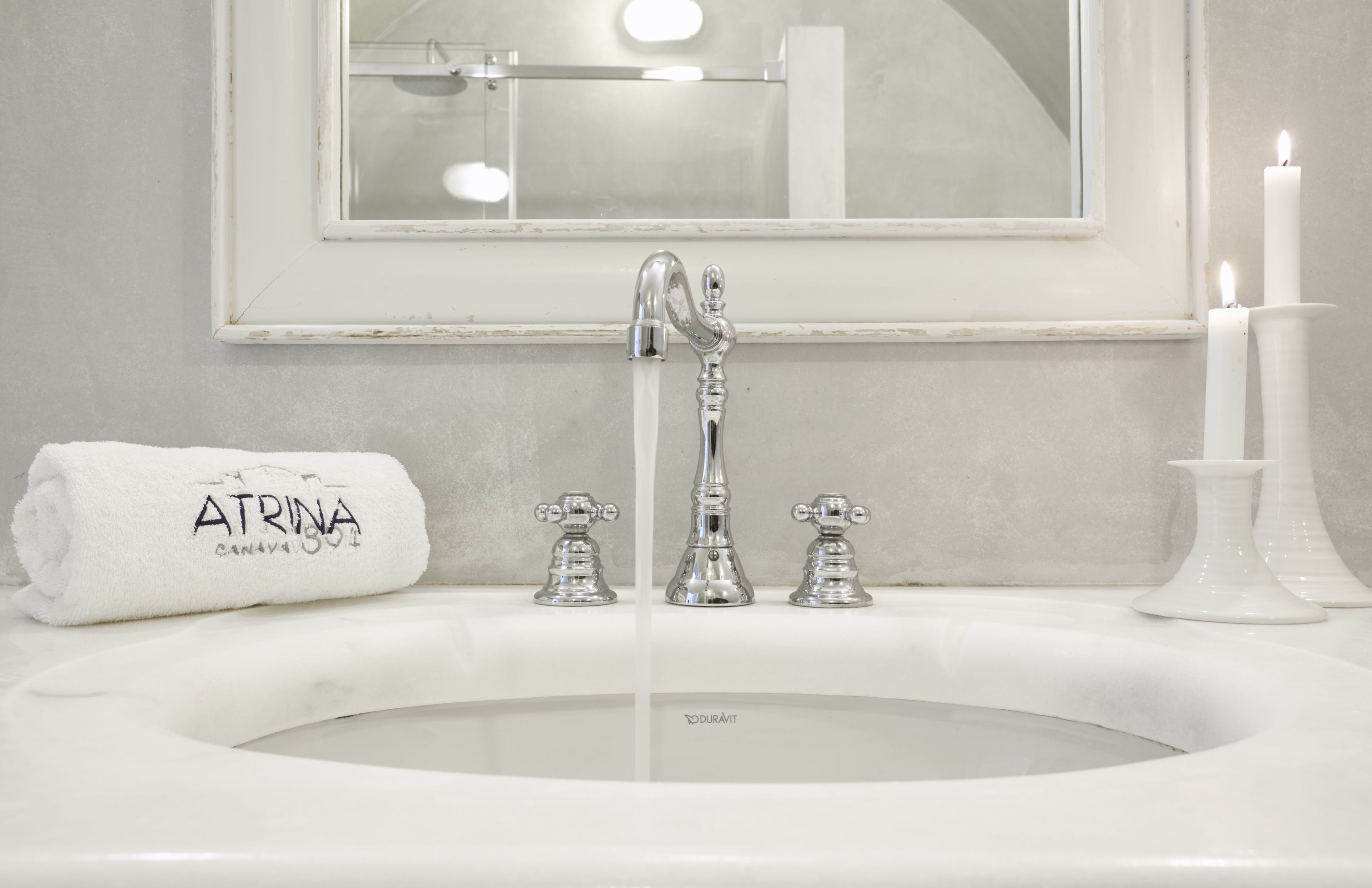 A bathroom with a white sink, a mirror above it, and two lit candles.