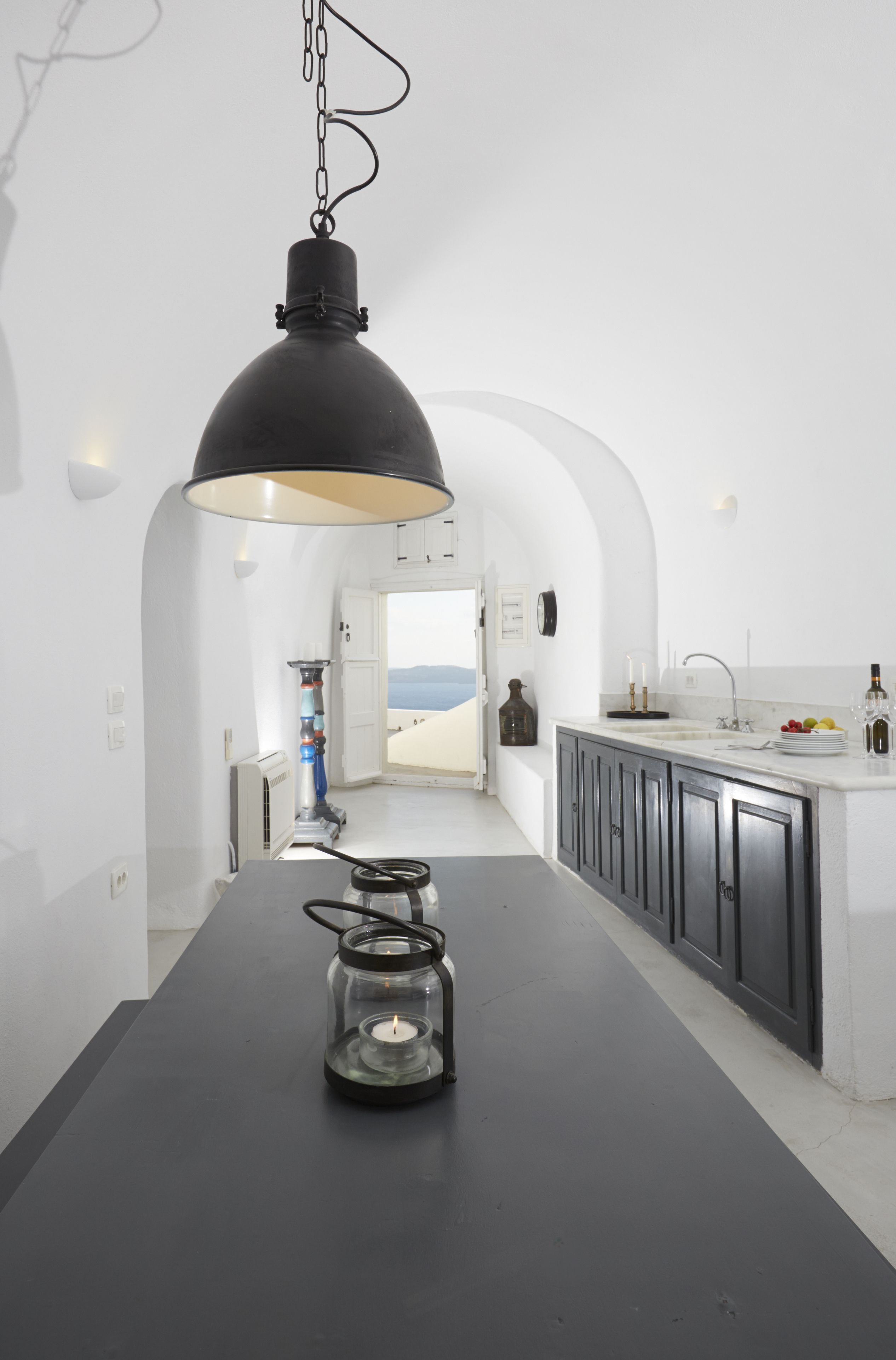 Una cocina moderna con una lámpara colgante negra, un candelabro de vidrio y vistas al paisaje desértico a través de una puerta abierta.