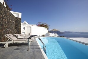 A poolside area with lounge chairs, a pool, and a view of the sea. - Atrina Canava 1894 (Santorini)