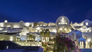 A coastal hotel with white domed architecture, outdoor seating, and a stone wall. - Atrina Canava 1894 (Santorini)