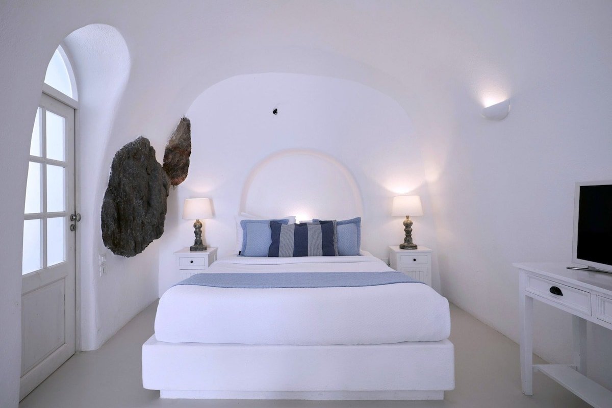 A bedroom with a large bed, two bedside tables with lamps, a television on a stand, and a large rock decoration on the wall.