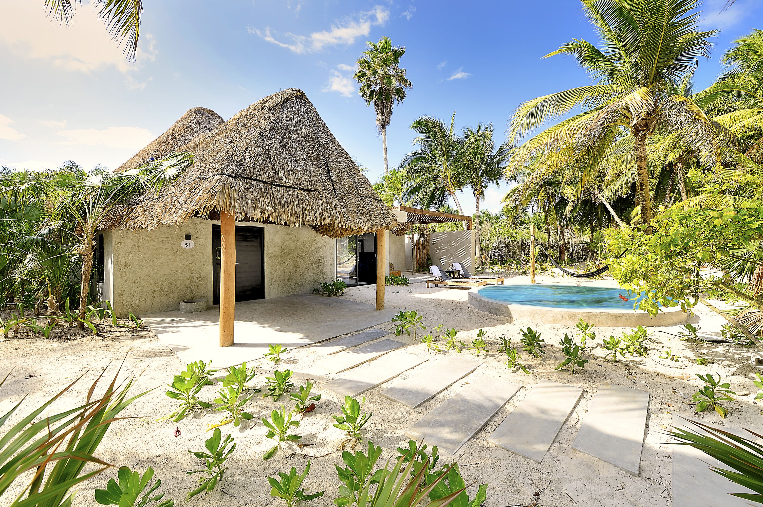 A thatched-roof building with a pool and lounge chairs.
