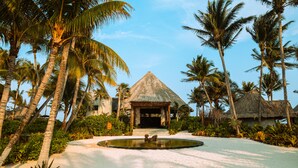 Un resort con una construcción de techo de paja, palmeras y una piscina.