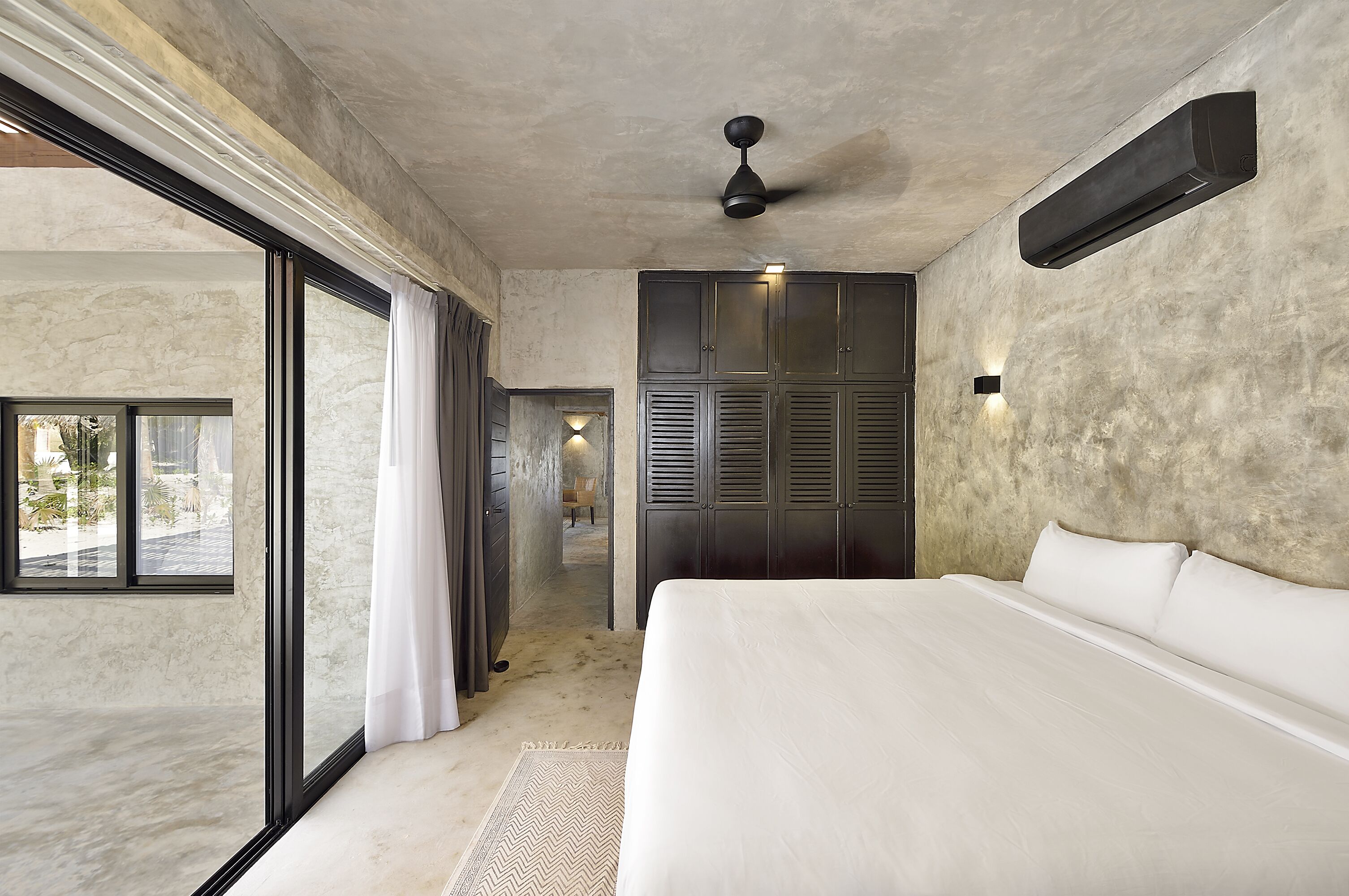 A bedroom with a large bed, a ceiling fan, and a view through a sliding door to an outdoor area.