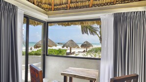 Una habitación con vista a una playa, techo de paja y una mesa de madera.