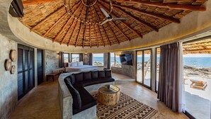 A circular room with a thatched roof, a large bed, a sofa, a TV, and a view of the beach. - Maya Tulum by G Hotels (Tulum)