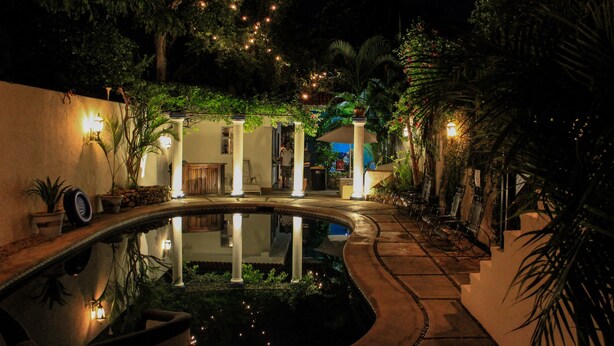 A nighttime pool area with a circular pool, palm trees, and ambient lighting. - Hotel Zamna (Mérida)